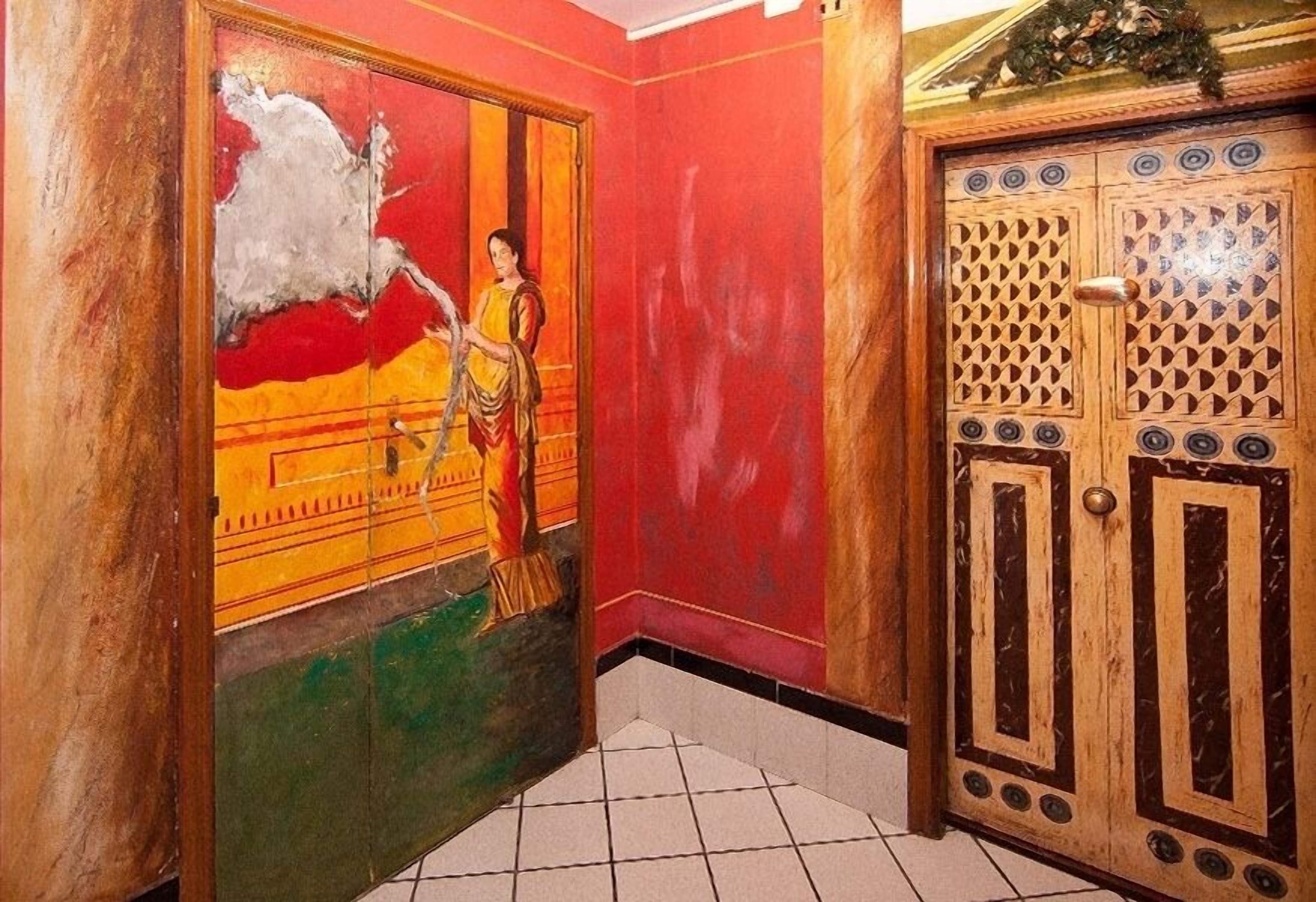 Un pasillo con un mural colorido a la izquierda y una puerta de madera con diseños intrincados a la derecha.