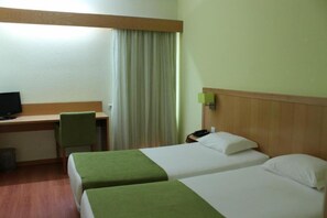 A hotel room with two beds, a desk, a chair, a television, and a lamp.