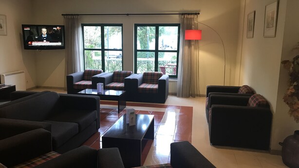 Una sala de estar moderna con televisor de pantalla plana, asientos cómodos, ventanas amplias y una lámpara roja en el suelo.
