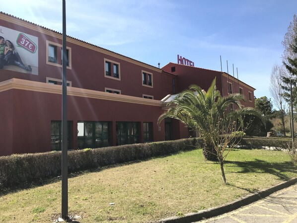 A red building with a 'HOTEL' sign, multiple windows, and a well-maintained lawn with a palm tree.
