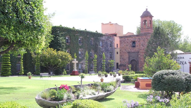 A courtyard with a fountain, neatly trimmed hedges, and a building with a bell tower.