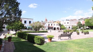 A courtyard with a bench, potted plants, and a building with a tower in the background.
