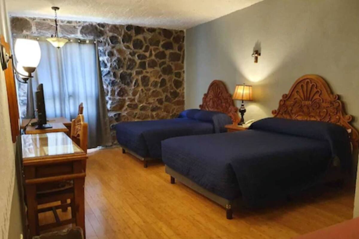 A room with two beds, a wooden desk, a stone wall, and a chandelier.
