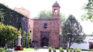 A historic building with a bell tower, surrounded by well-maintained gardens and a bench.