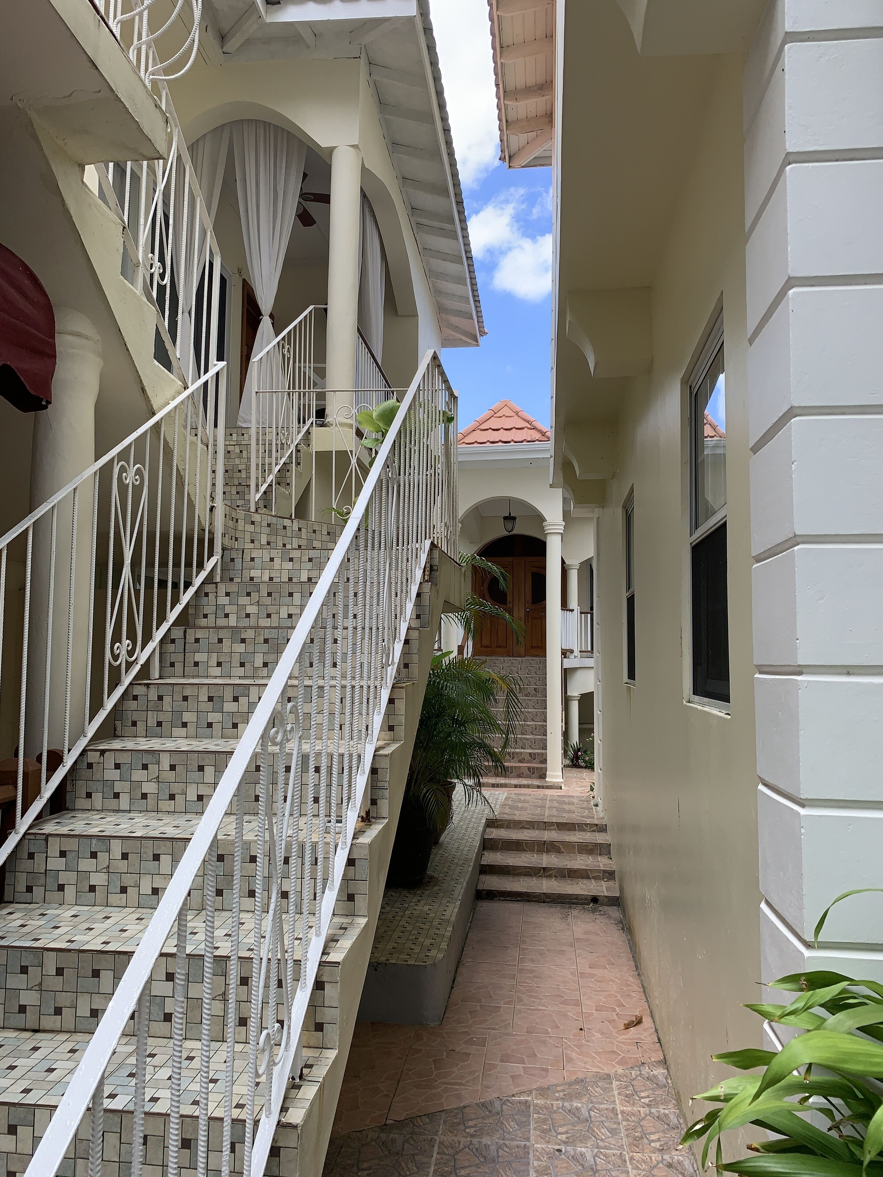 A narrow outdoor corridor with a tiled staircase leading to a covered area with a red-tiled roof.