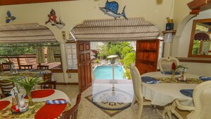 Comedor con mesas dispuestas para recibir a los huéspedes, vista a la piscina y decoración tropical.
