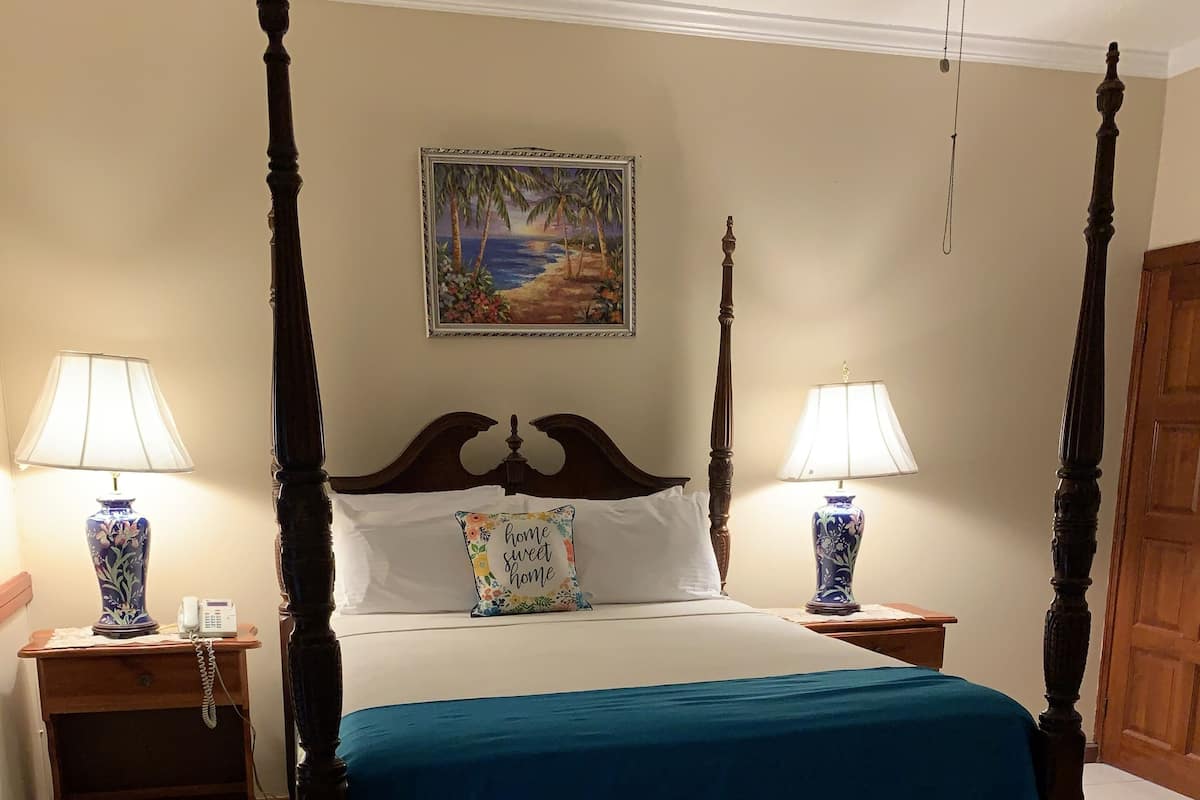 Una cama con dosel con colcha azul, dos mesitas de noche con lámparas, un banco de madera y un cuadro en la pared.