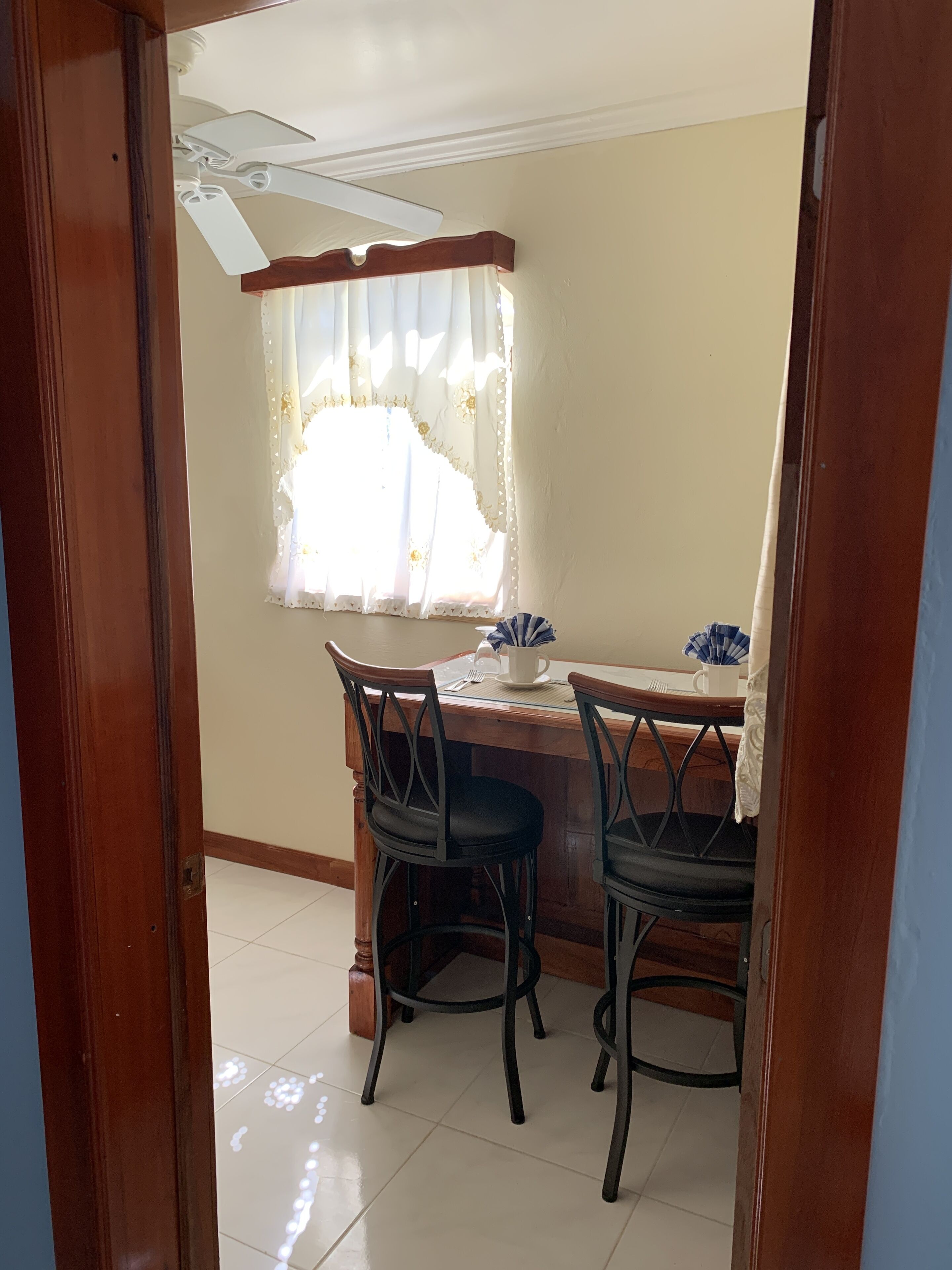 A dining area with a wooden table and two chairs, a ceiling fan, and a window with curtains.