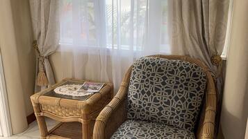Un sillón de mimbre con un cojín estampado, una mesita de mimbre con un bordado de encaje, y una alfombra estampada sobre un suelo de baldosas.