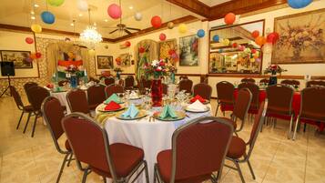 A banquet hall with round tables set for dining, chairs, and a chandelier.