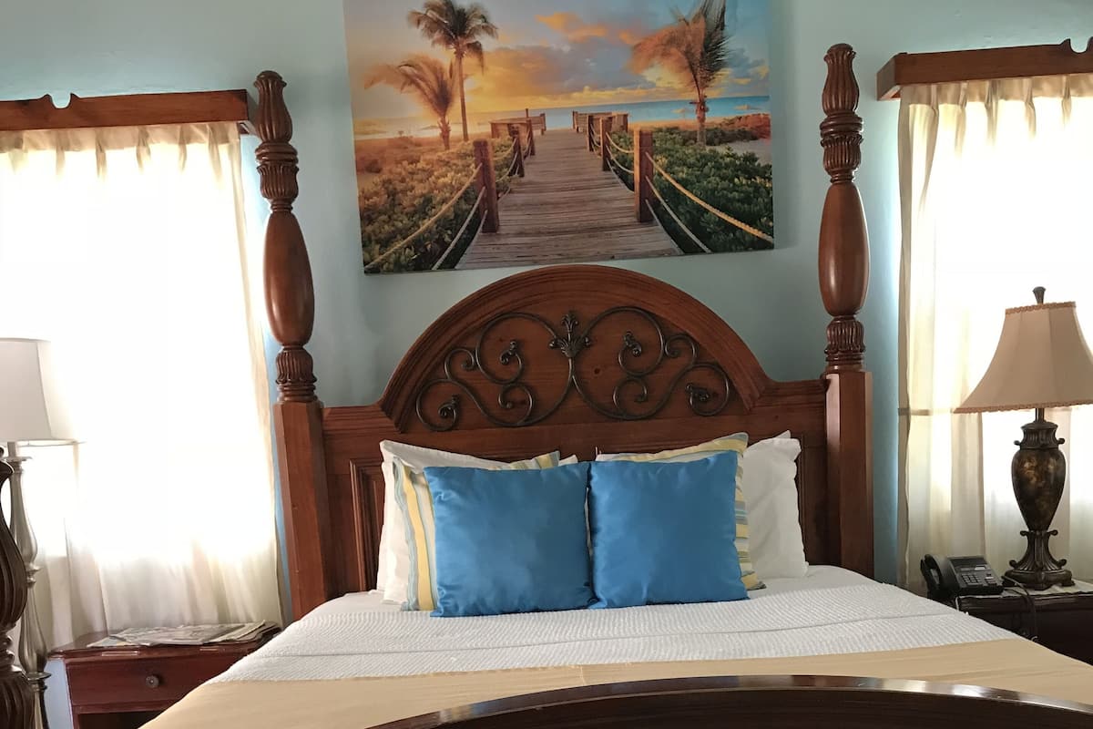 Una cama de madera con cabecera, un cuadro de una escena de playa y una lámpara sobre una mesita de noche.