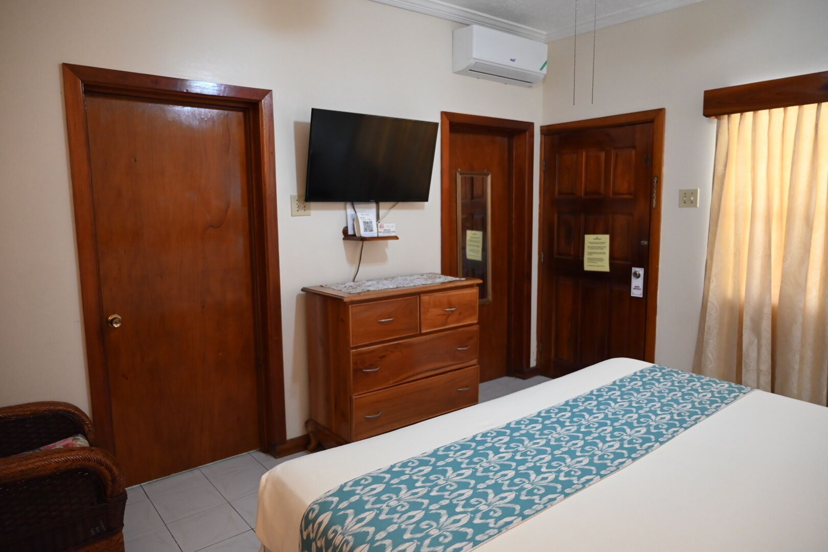 A hotel room with a bed, a wooden dresser, a television, and a wardrobe.