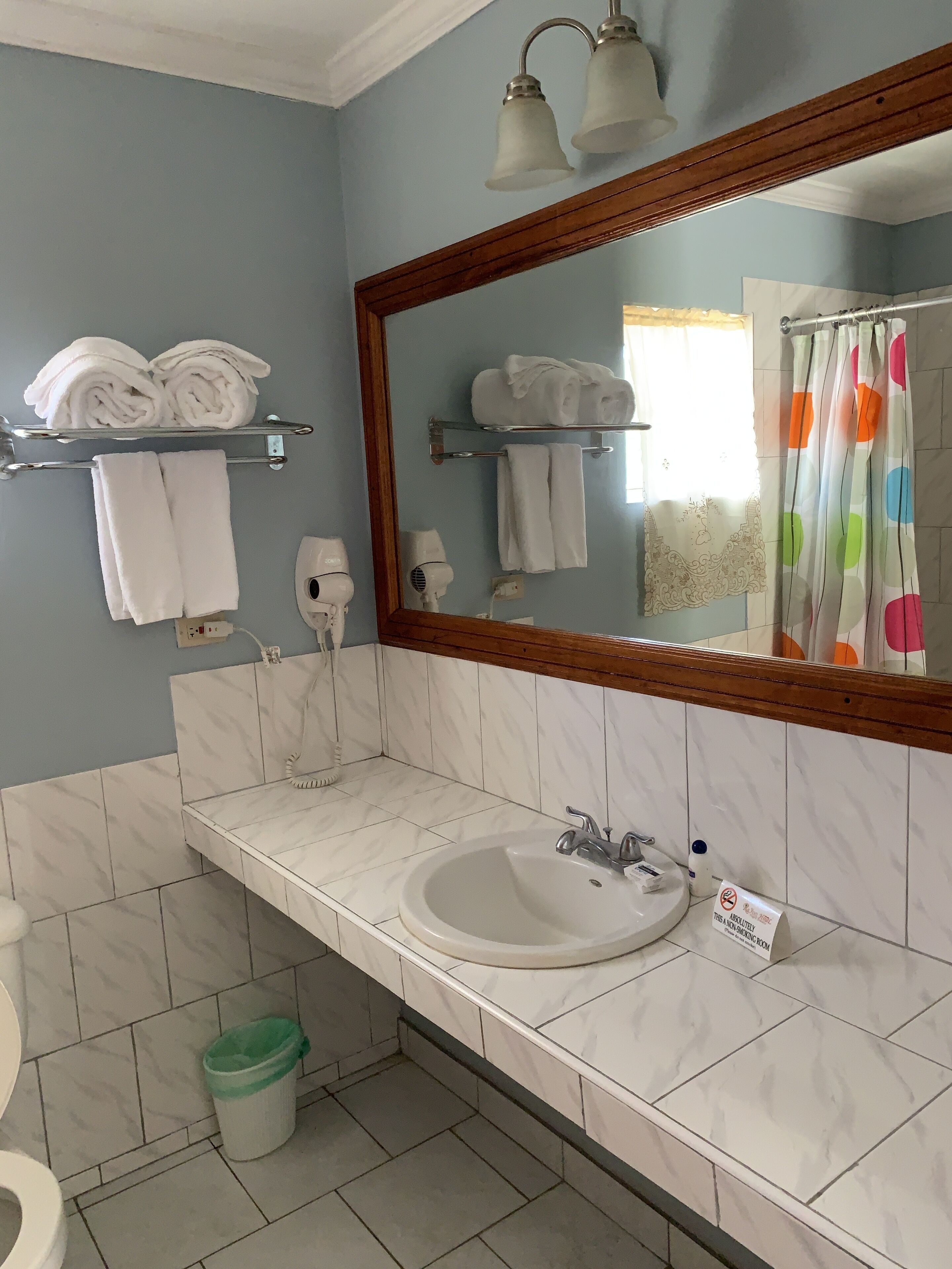 A bathroom with a sink, mirror, towel racks, and a shower curtain.