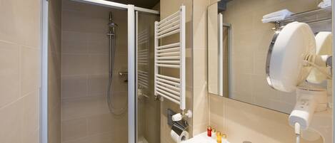 A modern bathroom with a glass shower enclosure, a white towel rack, a sink with a mirror, and a hairdryer on the countertop.