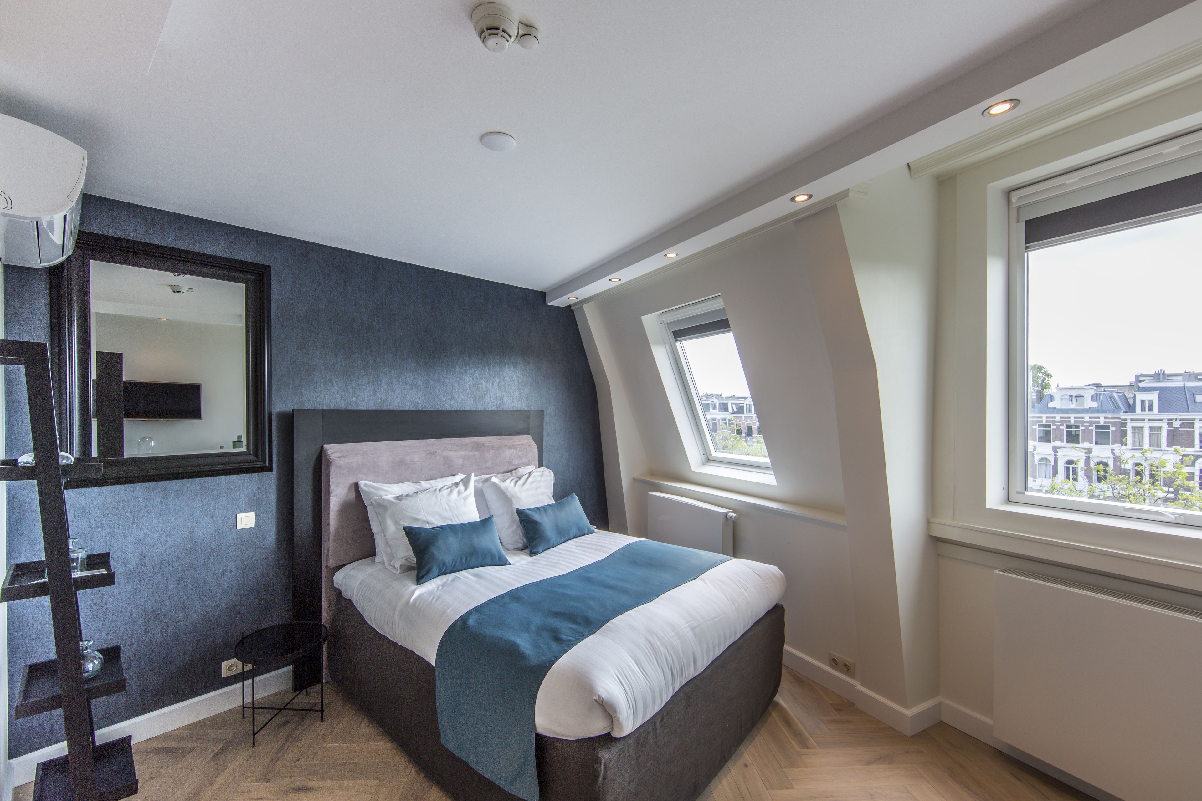 A modern bedroom with a large bed, a skylight, and a city view.