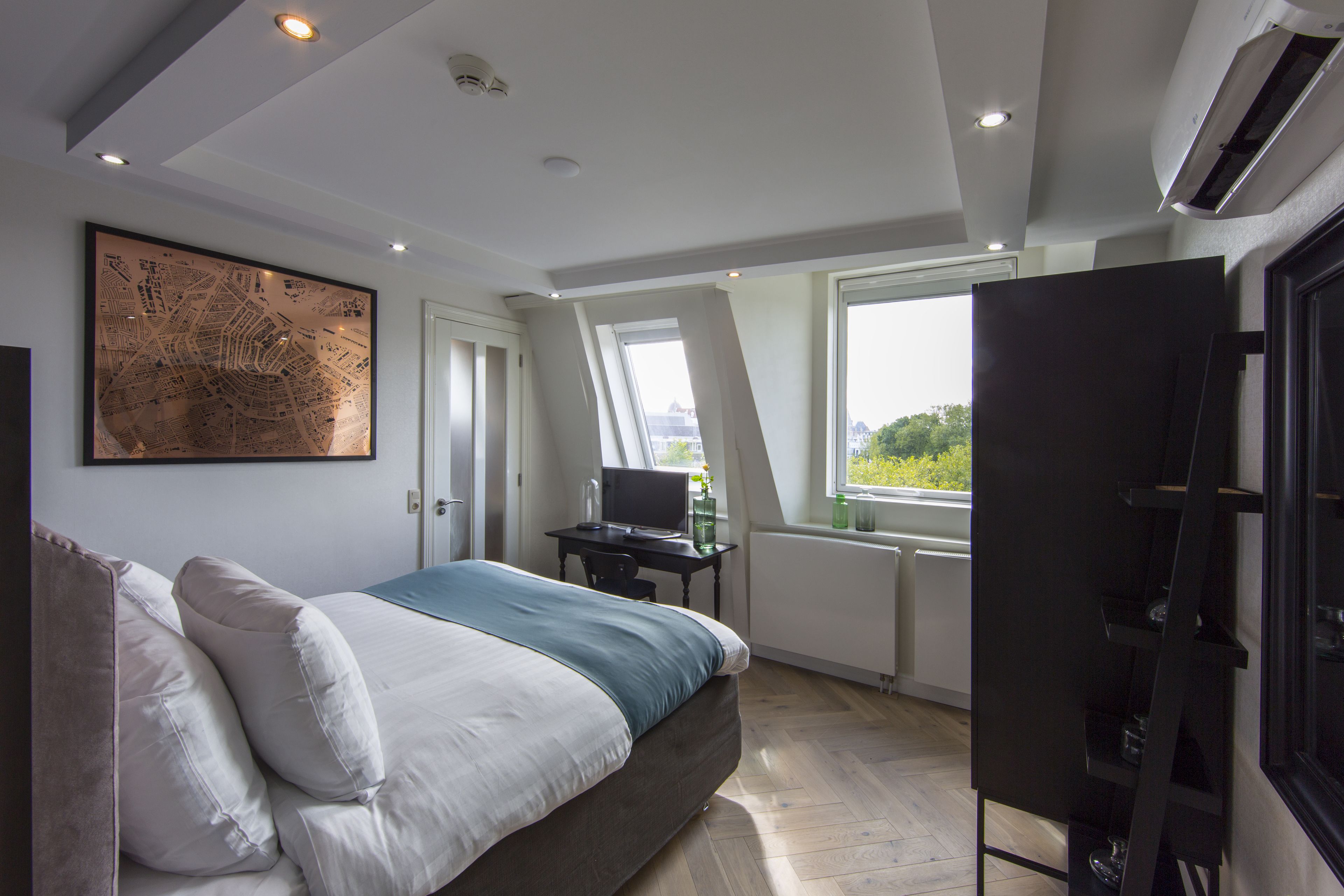 A bedroom with a bed, a desk, and a large window.
