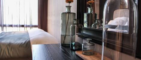 A neatly arranged hotel room with a bed, a wooden side table, and a mirror reflecting the room's decor.