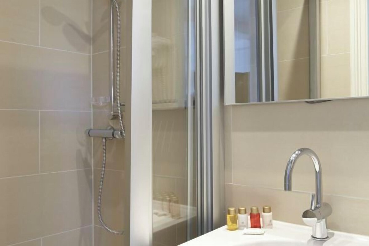 A modern bathroom with a glass shower enclosure, a sink with a chrome faucet, and a mirror.
