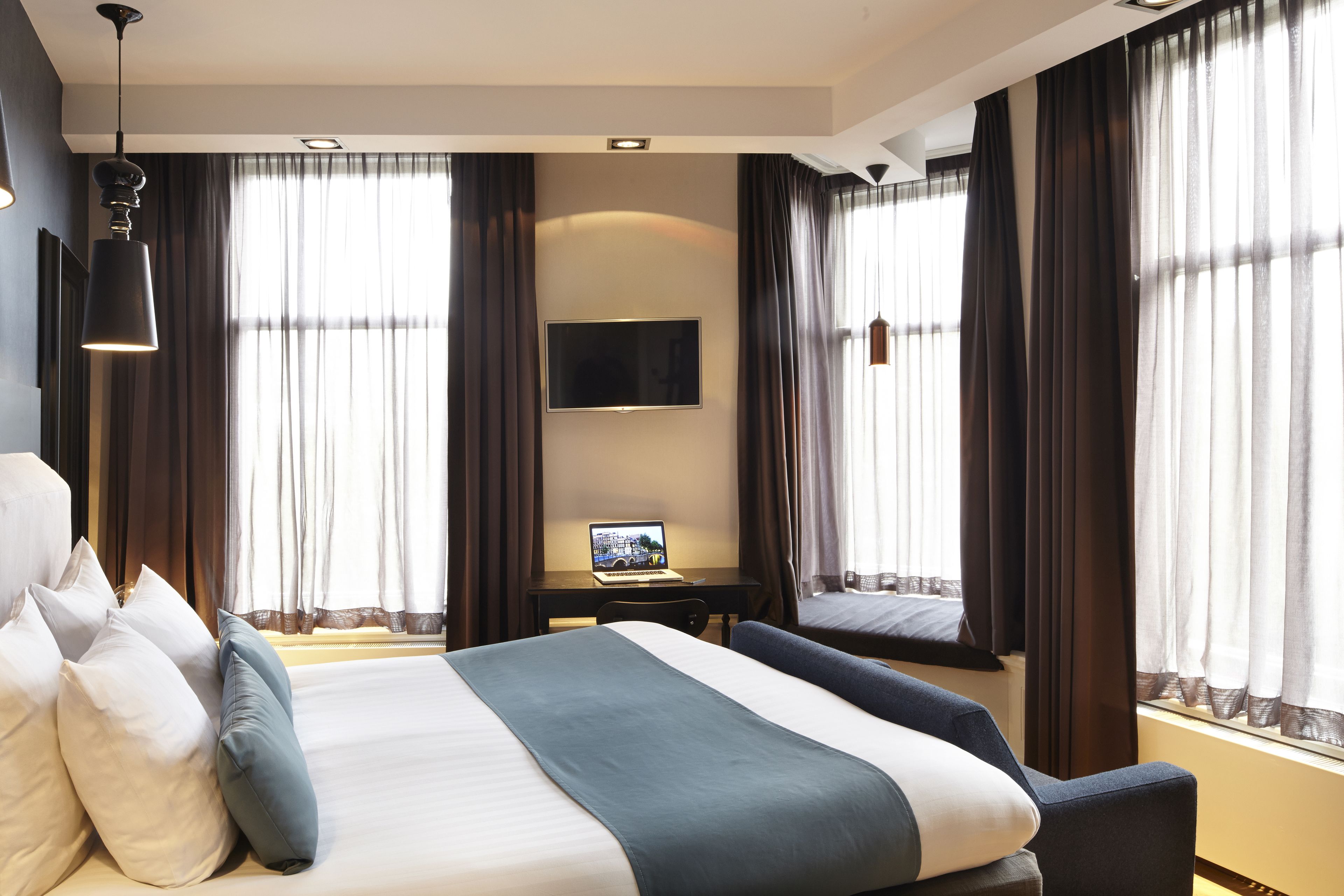A hotel room with a large bed, a desk with a laptop, and a TV mounted on the wall.