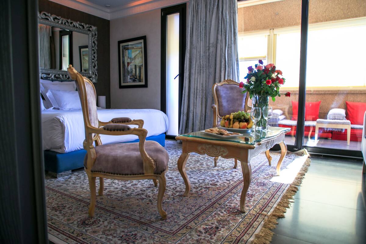 Ein Hotelzimmer mit Bett, Stuhl, Tisch mit Früchten und einer Vase sowie Blick ins Freie.