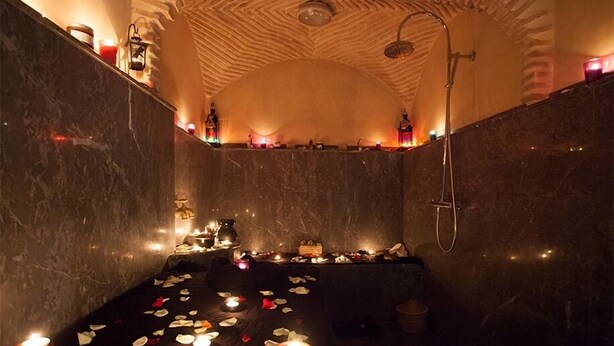 A spa room with a stone wall, a bathtub, candles, and a shower. - Medina Loft & Spa (Marrakech)