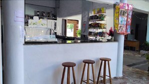Um pequeno bar com banquetas, balcão e prateleiras repletas de petiscos.