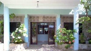 Fachada de um edifício com azulejos, porta central e vegetação ao redor.