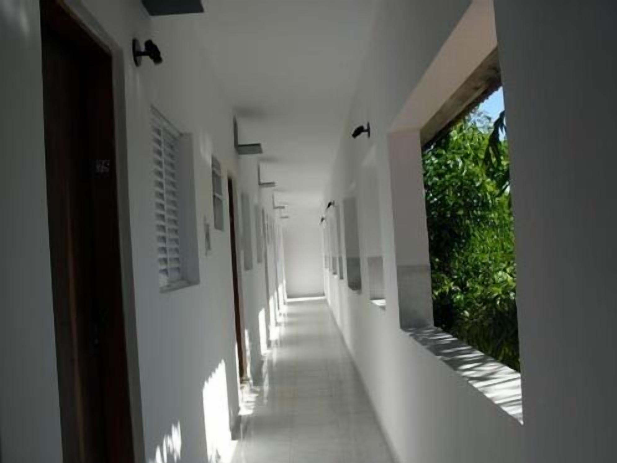 Un pasillo largo y estrecho con paredes blancas y puertas a la izquierda, que conduce a habitaciones.