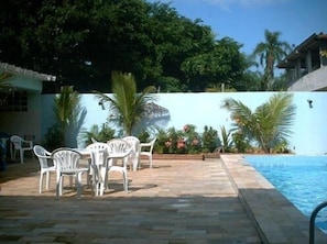 A pool area with white plastic chairs and a table, surrounded by palm trees and a blue wall.