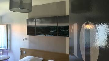 Habitación de hotel con cama, una mesa redonda y una obra de arte colgada en la pared que representa un mar embravecido.
