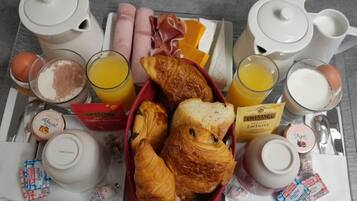 A breakfast tray with croissants, ham, orange juice, and a variety of condiments.