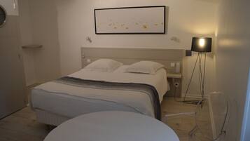 Een hotelkamer met een bed, nachtkastje, lamp en een ingelijst schilderij aan de muur.