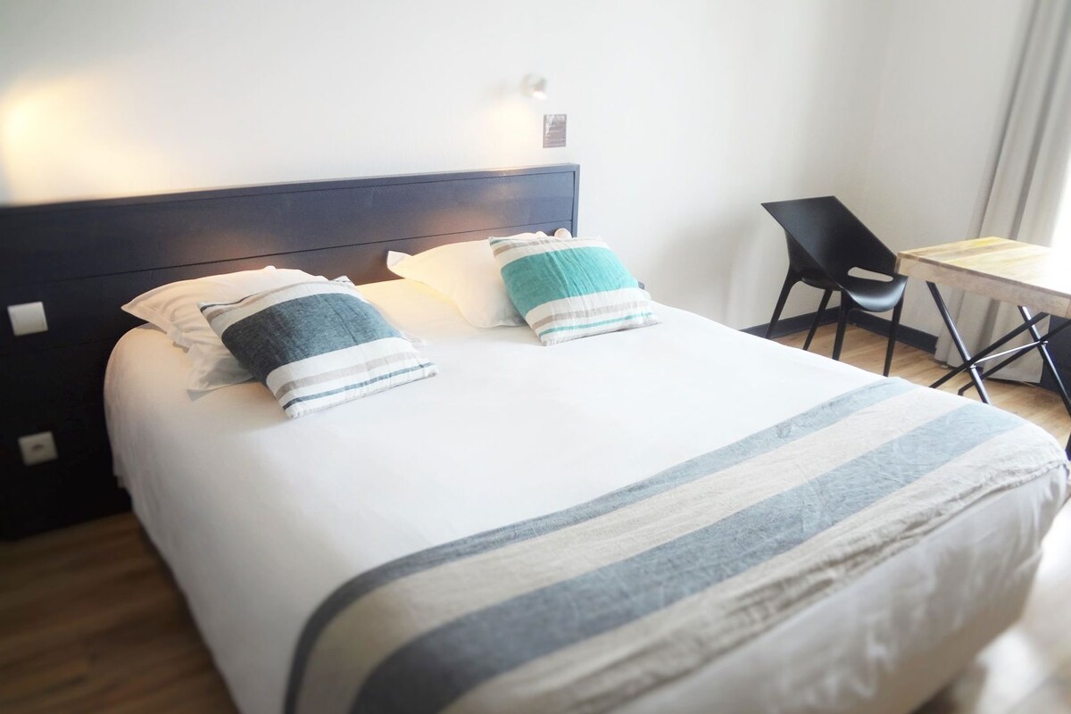 A neatly made bed with striped bedding, a dark headboard, and a small table with a chair beside it.