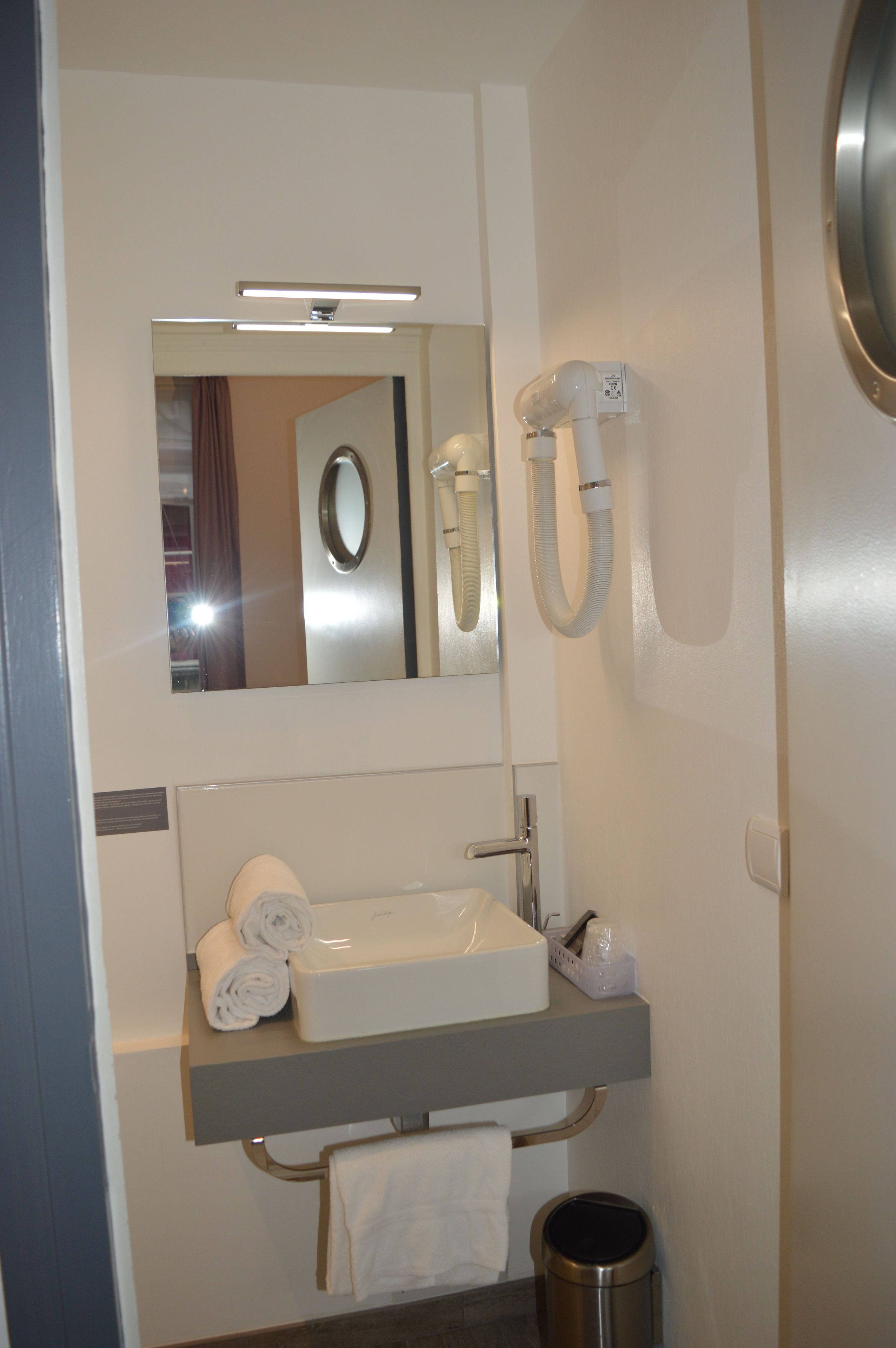 Un baño con lavamanos, espejo, toallero y cubo de basura.