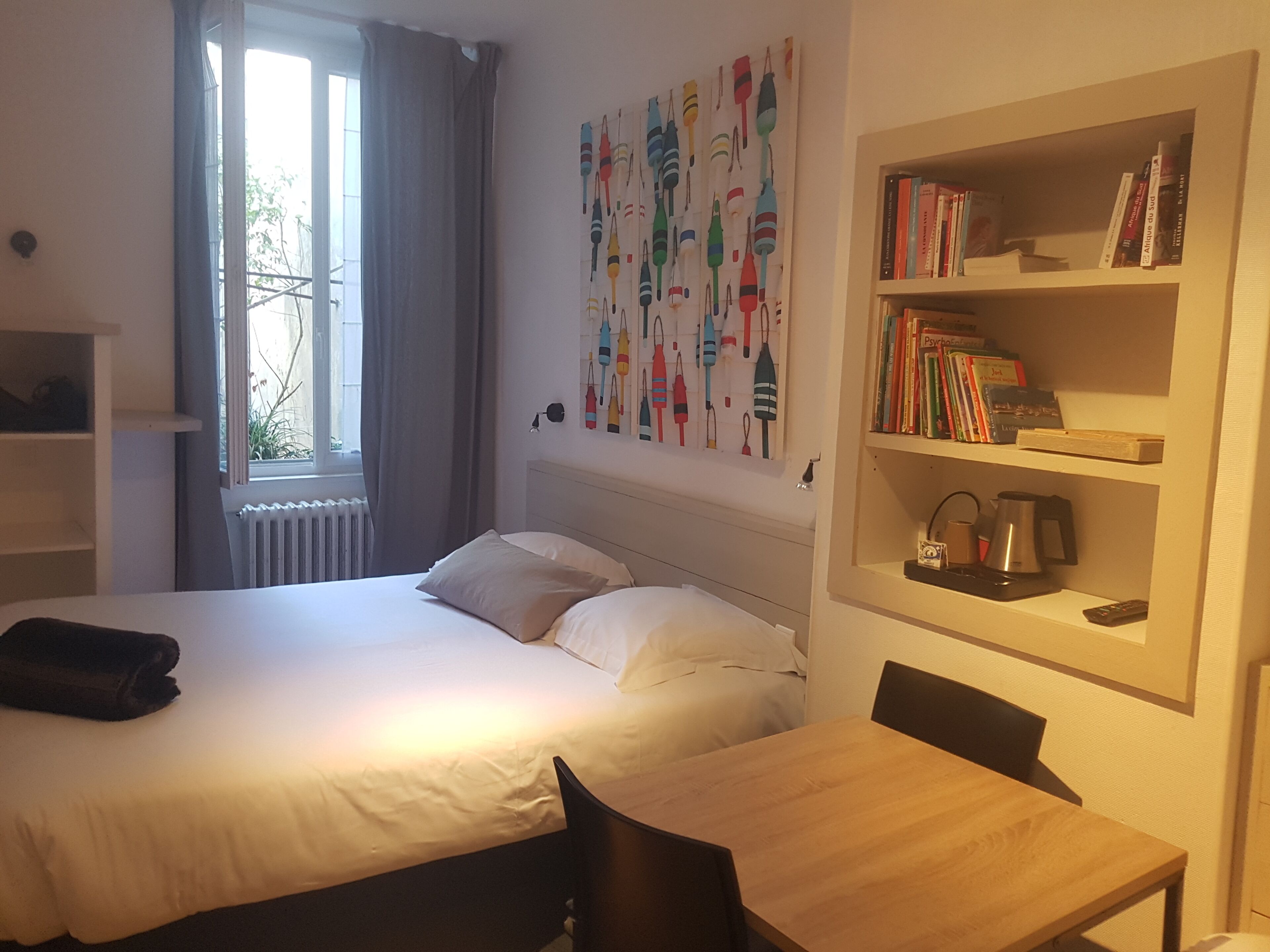 Een slaapkamer met een bed, nachtkastje, een boekenkast en een raam met gordijnen.