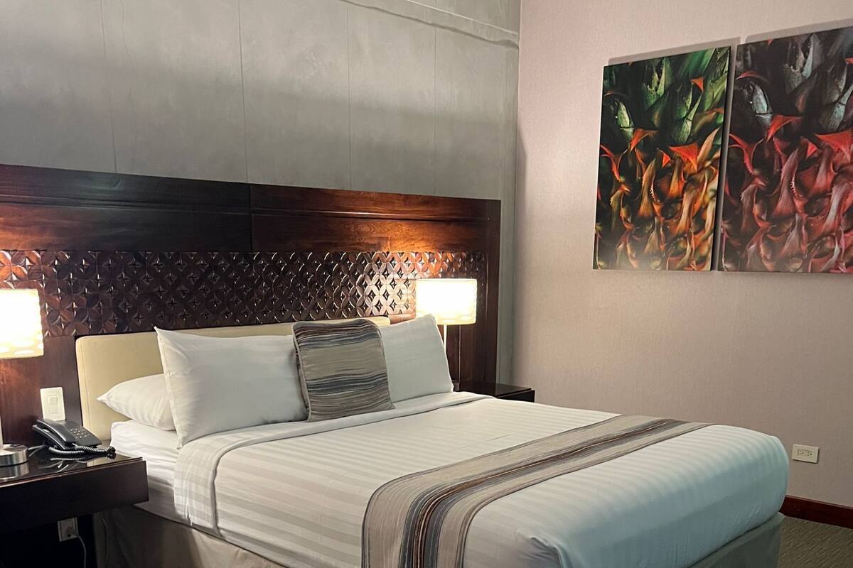 A hotel room with a large bed, two bedside lamps, a telephone, and a decorative headboard.