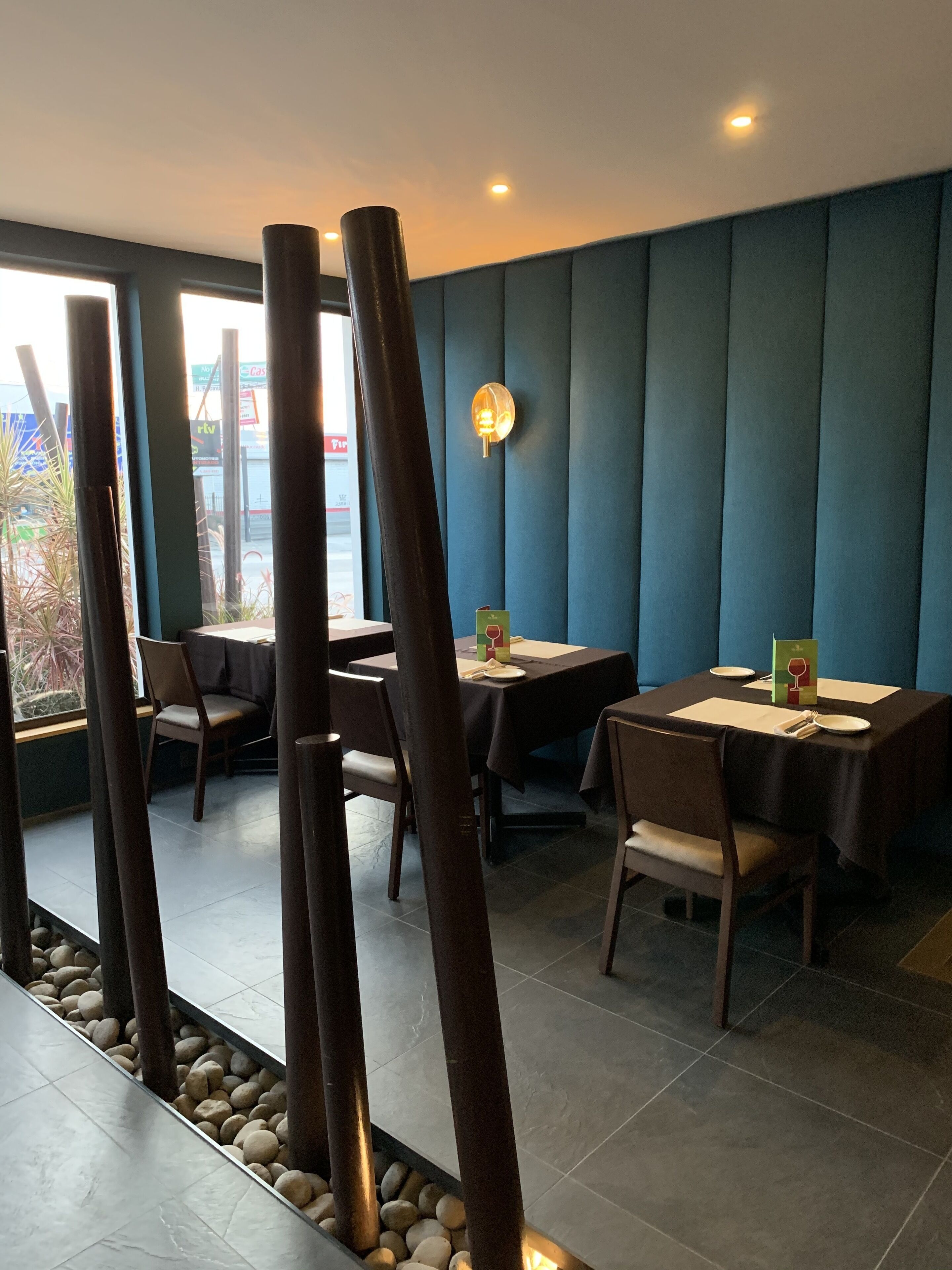 Interior de restaurante con mesas y sillas, una lámpara decorativa en la pared y vistas al exterior a través de amplias ventanas.