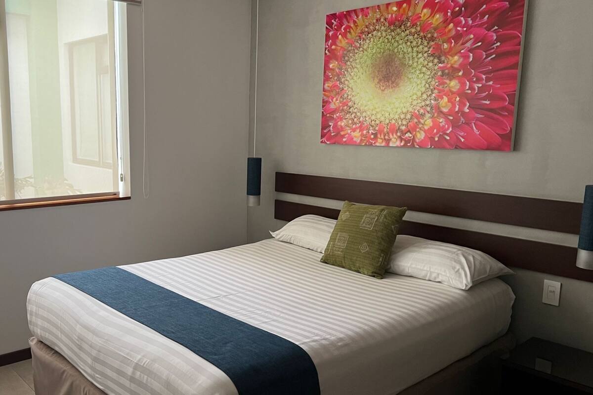 A neatly made bed with a blue and white striped bedspread, a green pillow, and a white pillow. A large floral artwork is on the wall above the bed.
