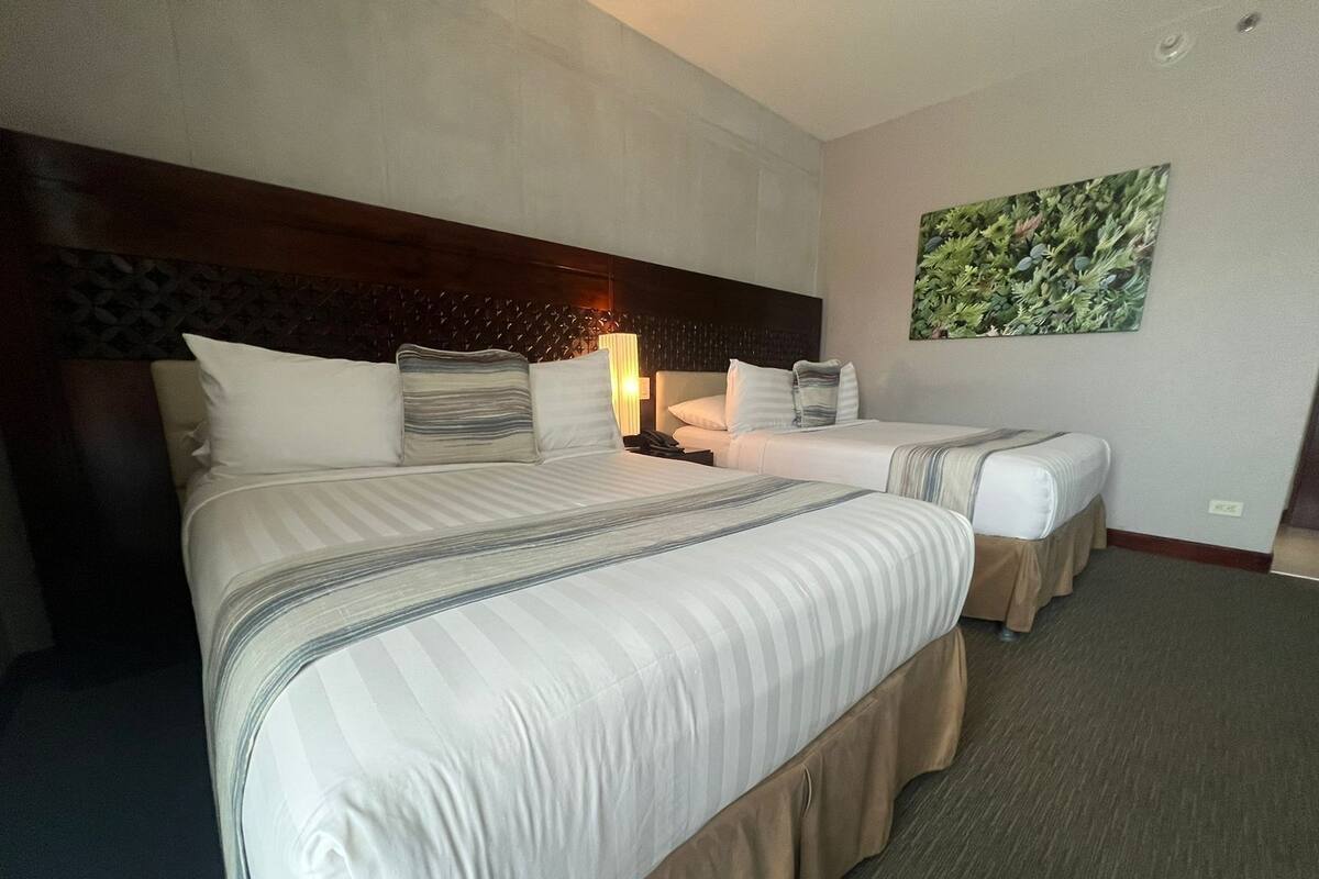 A hotel room with two beds, a headboard, a nightstand, a lamp, and a wall-mounted artwork.