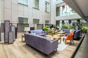 Un hall espacioso con un sofá grande, sillones y una mesa de centro. Se observan separadores decorativos y plantas en macetas.