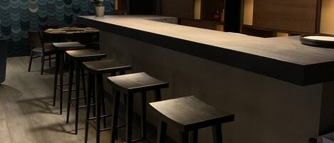 Zona de bar moderna con techo de madera, mostrador con taburetes y pared con diseño.