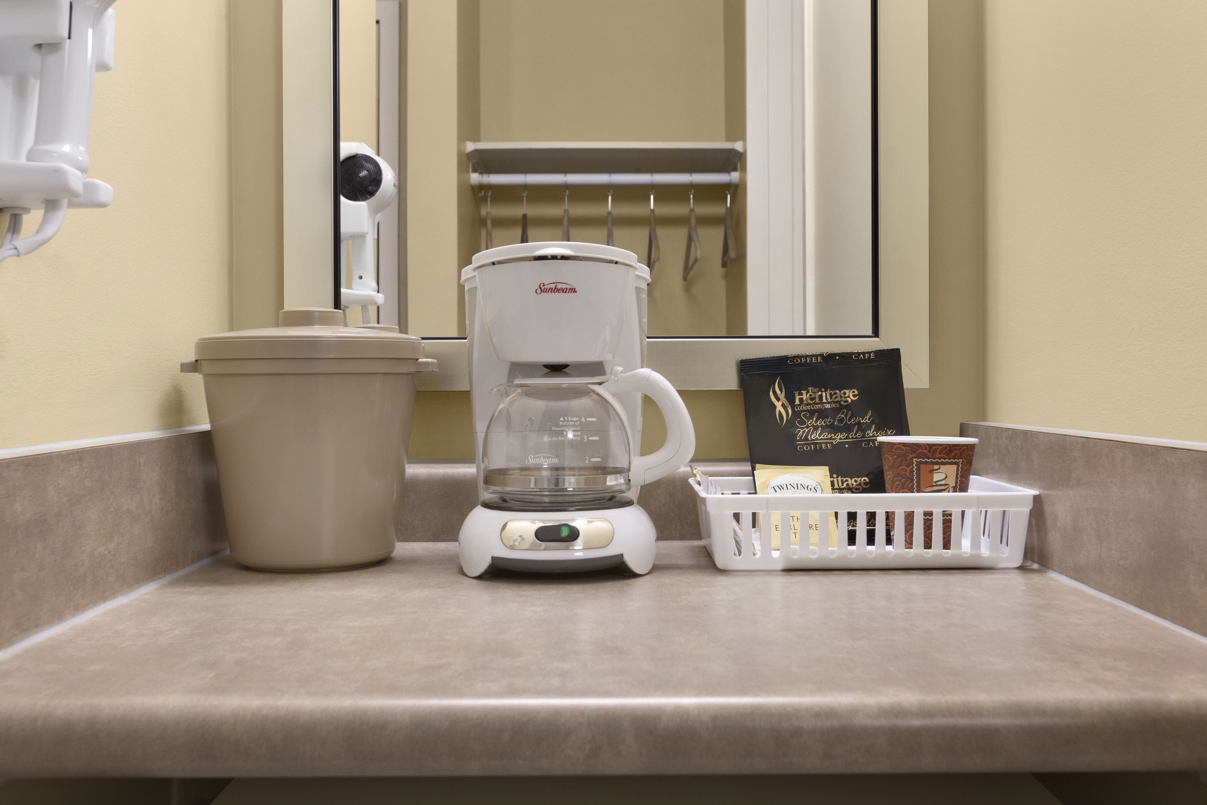 Una cafetera, un cesto de basura y una cesta con tazas de café sobre una encimera.