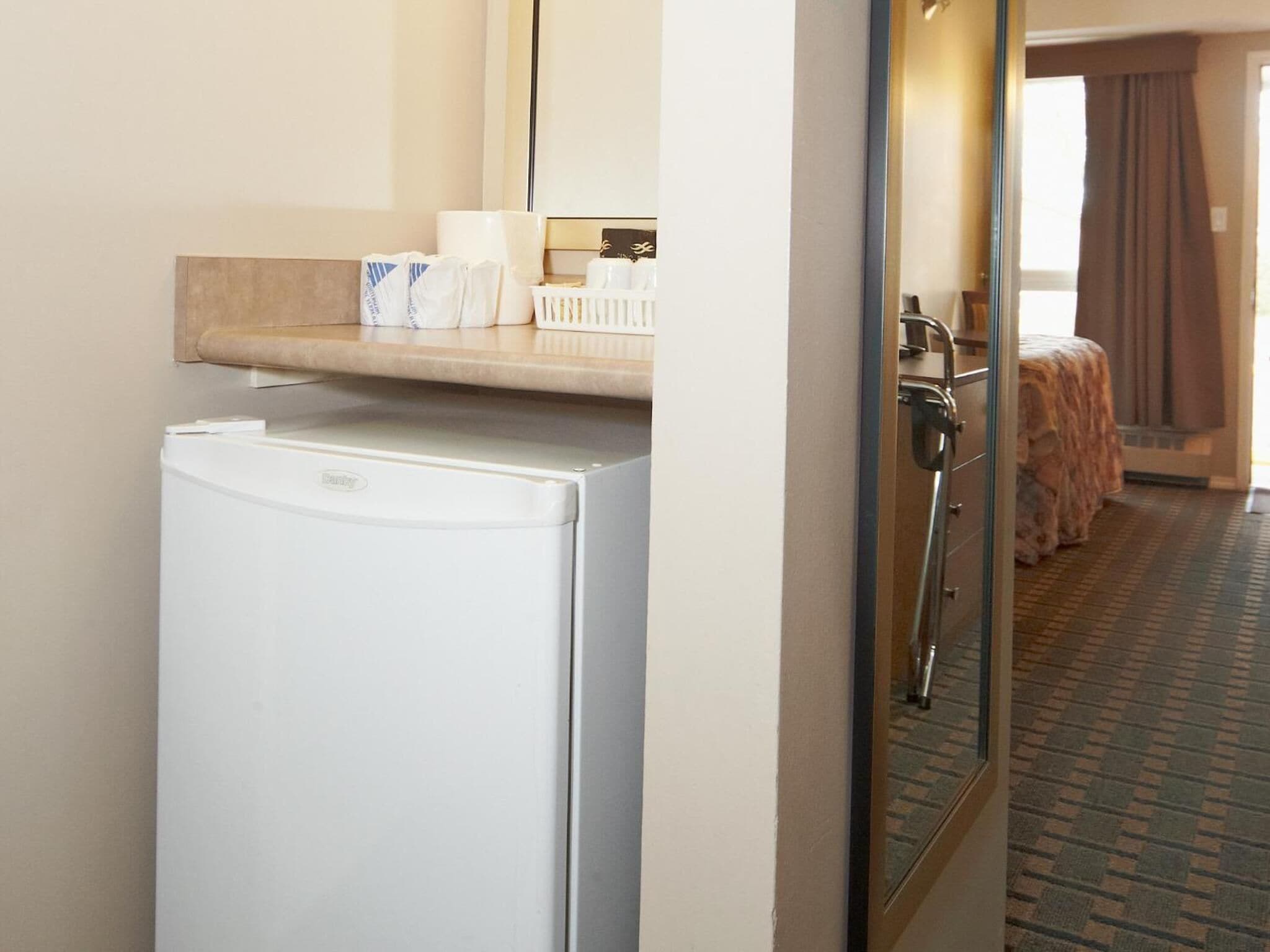 Ein Hotelzimmer mit Kühlschrank, einer kleinen Ablage mit Pflegeprodukten und einem Bett mit brauner Bettdecke.