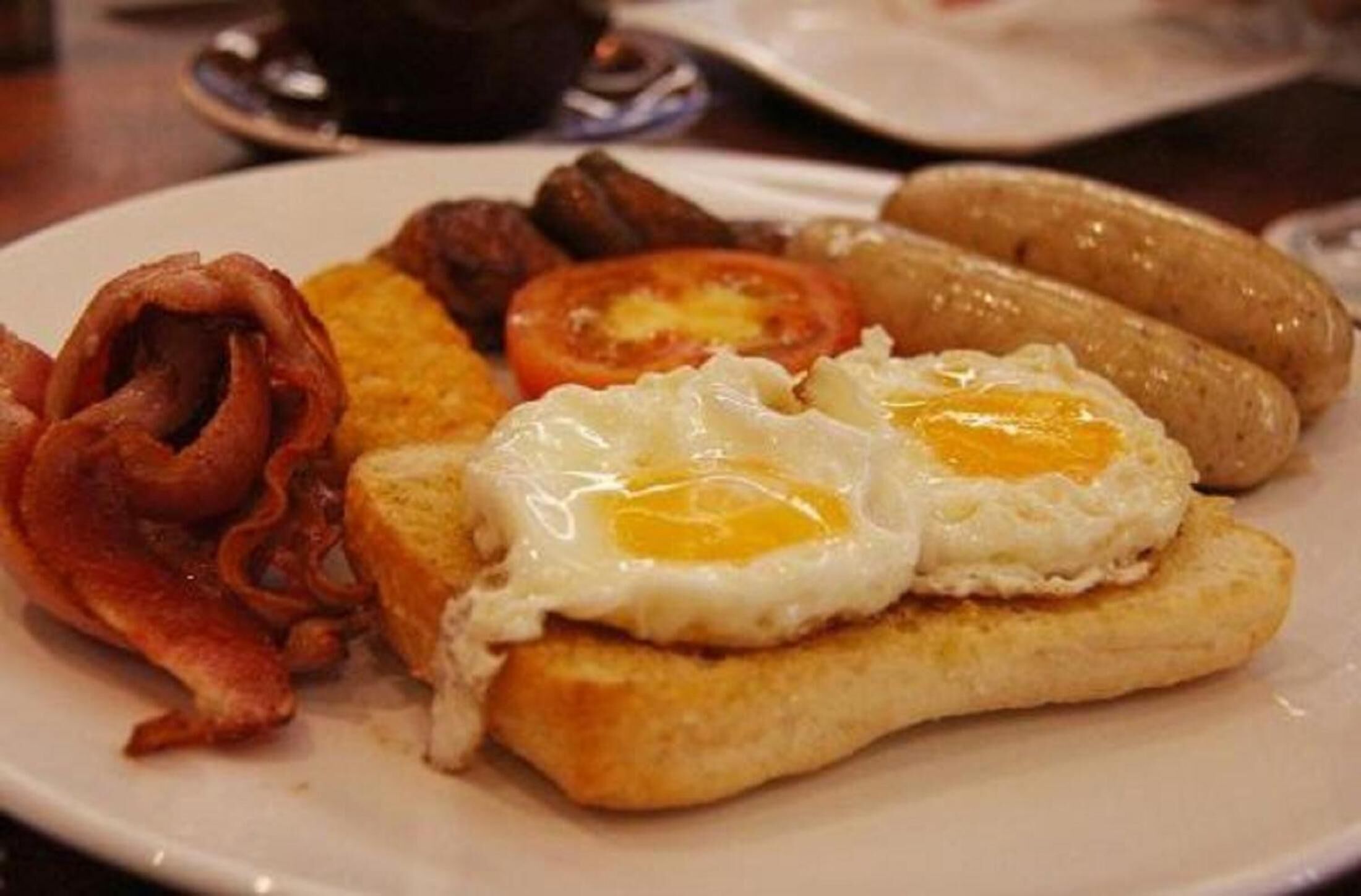 A plate of breakfast food including eggs, bacon, sausages, and toast.