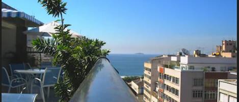 A narrow outdoor corridor with a view of the sea and buildings.