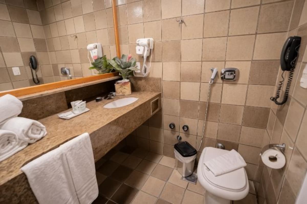 A bathroom with a sink, mirror, towel rack, toilet, and a telephone.