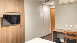 A hotel room with a wooden panel wall, a flat-screen TV mounted on it, a desk with a chair, and a small trash bin. - Stop Inn Cristiano Machado (Belo Horizonte)
