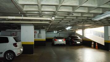 A parking garage with concrete pillars, overhead pipes, and a fire extinguisher.