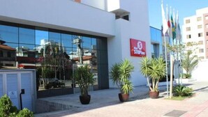 A modern building with a glass facade, a red sign with white text, and several potted plants in the foreground. - Stop Inn Cristiano Machado (Belo Horizonte)