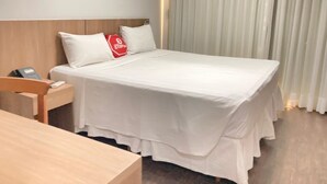 A hotel room with a neatly made bed, a wooden nightstand with a phone, and a red stop sign pillow. - Stop Inn Cristiano Machado (Belo Horizonte)